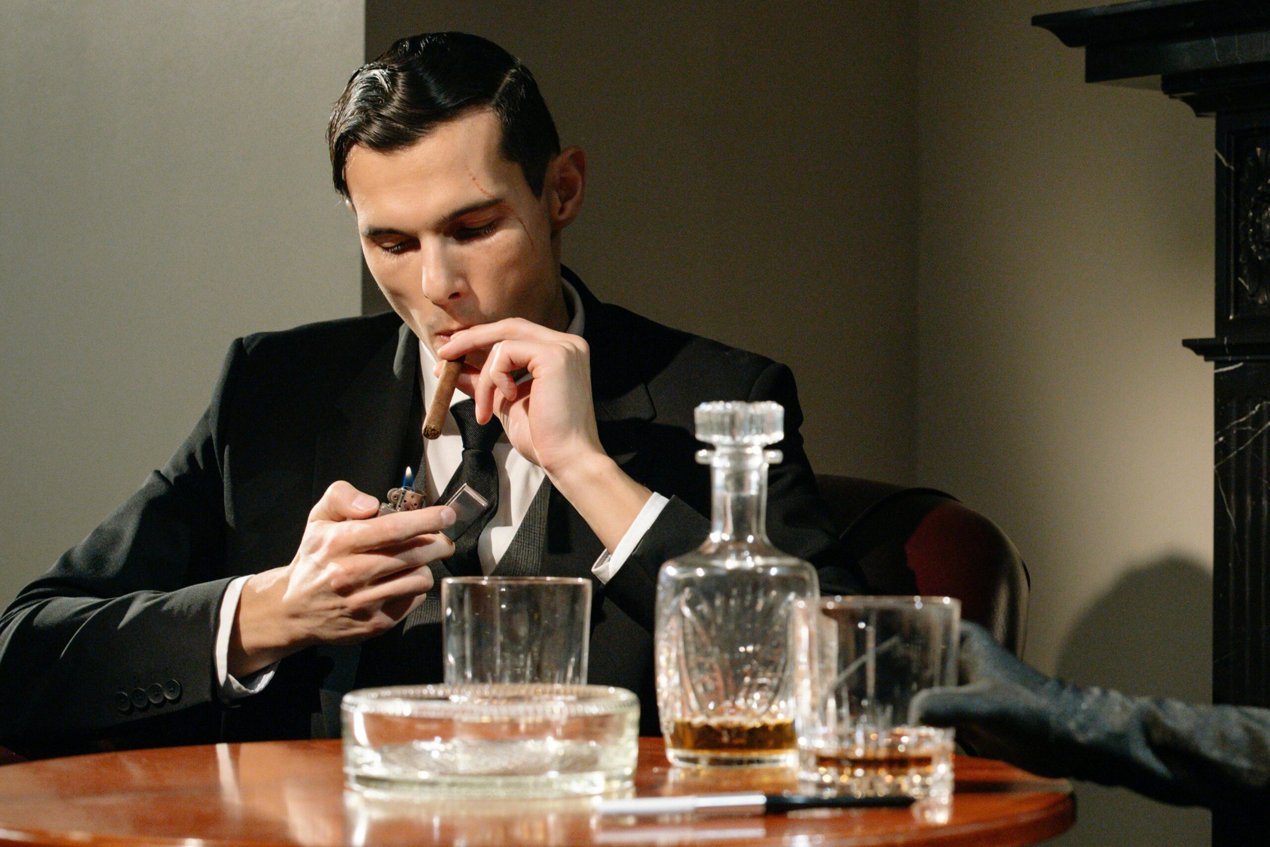 A sophisticated man in a suit smokes a cigar while enjoying a drink, exuding luxury and vintage style.